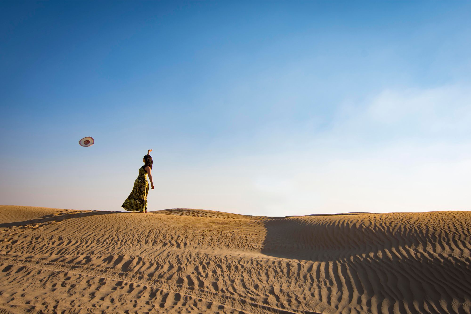 Traveler on sand dunes throwing a hat into the air